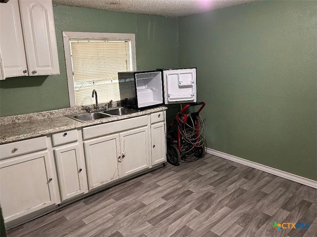 kitchen with a textured ceiling, hardwood / wood-style flooring, white cabinetry, and sink