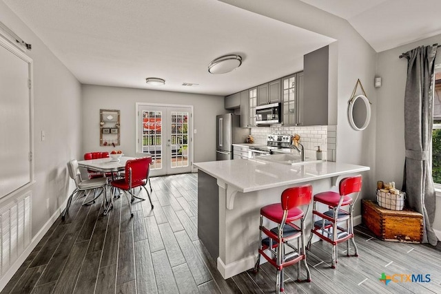 2075 Sungate Dr, New Braunfels, TX 78130 - kitchen featuring stainless steel appliances, gray cabinetry, wood finished floors, and a breakfast bar area
