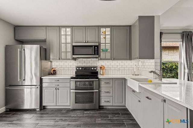 2075 Sungate Dr, New Braunfels, TX 78130 - kitchen with appliances with stainless steel finishes, gray cabinets, glass insert cabinets, and decorative backsplash