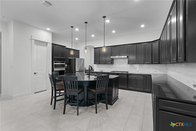 kitchen featuring appliances with stainless steel finishes, hanging light fixtures, an island with sink, a breakfast bar, and backsplash