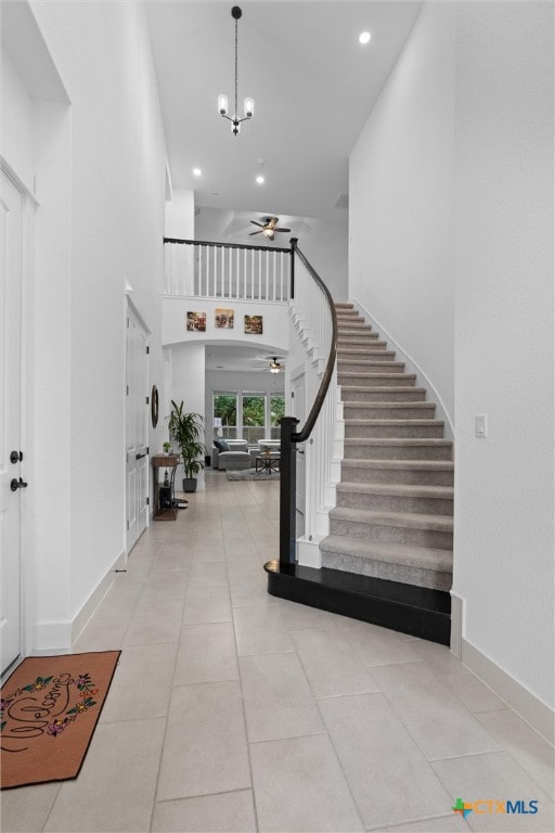 foyer entrance with ceiling fan with notable chandelier, light tile patterned floors, and a towering ceiling