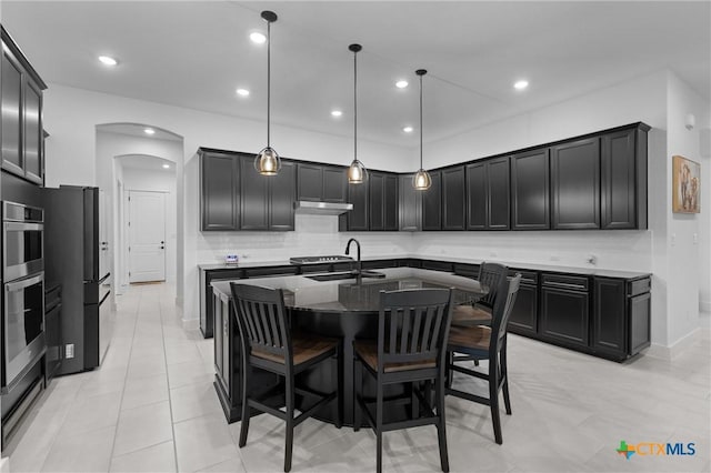 kitchen featuring a kitchen island with sink, decorative light fixtures, sink, backsplash, and black fridge