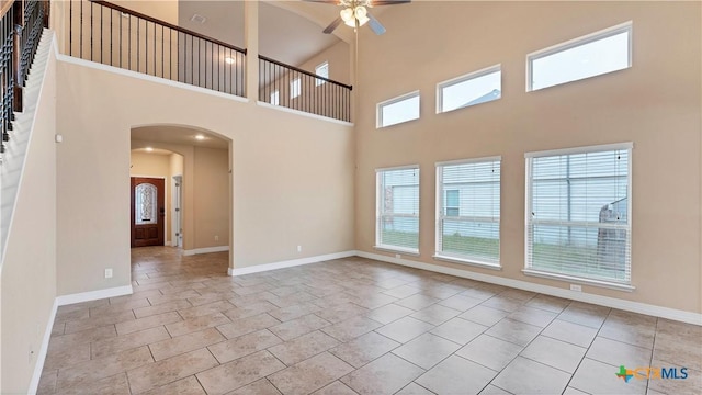 tiled empty room featuring ceiling fan, a healthy amount of sunlight, and a towering ceiling