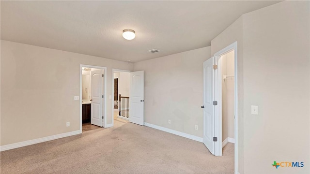 unfurnished bedroom featuring ensuite bath, light colored carpet, a spacious closet, and a closet