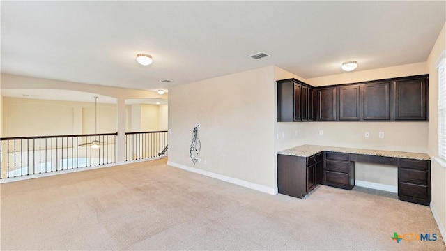 interior space with light stone countertops, dark brown cabinets, built in desk, and light colored carpet