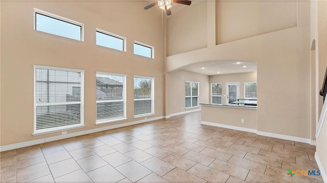 tiled empty room featuring ceiling fan and a towering ceiling