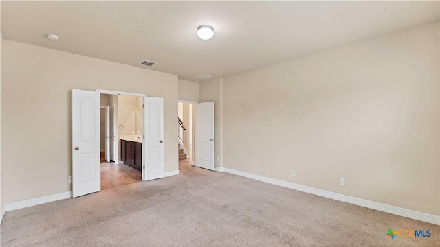 unfurnished bedroom featuring light colored carpet and ensuite bath