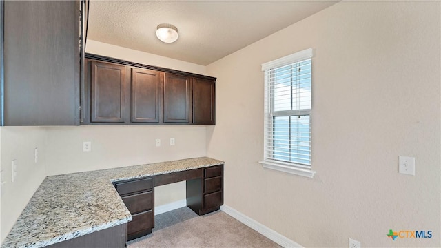 kitchen featuring dark brown cabinetry, light stone countertops, and built in desk