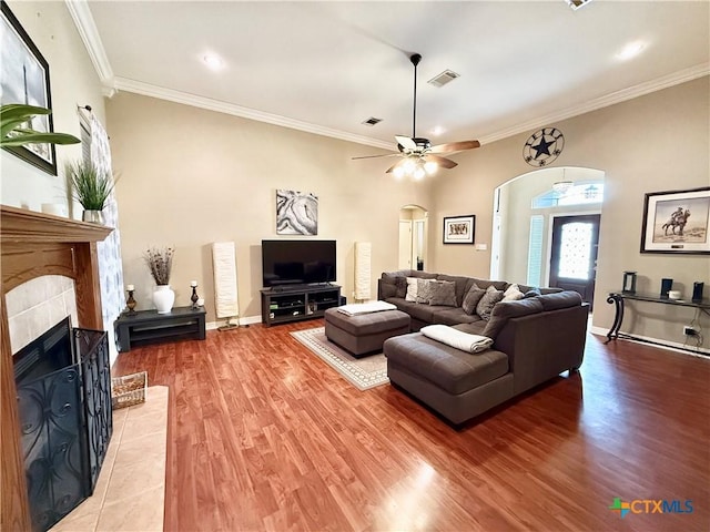 living room featuring a tiled fireplace, hardwood / wood-style flooring, crown molding, and ceiling fan