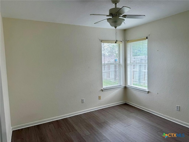 unfurnished room with dark wood-type flooring, a wealth of natural light, ceiling fan, and baseboards
