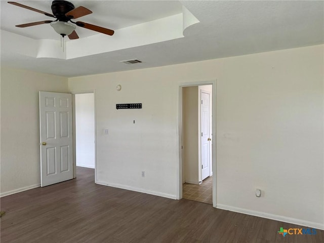 empty room with visible vents, baseboards, a ceiling fan, and dark wood-style floors