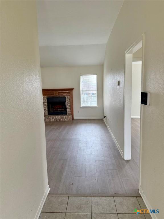 unfurnished living room featuring baseboards, a brick fireplace, a textured wall, wood finished floors, and lofted ceiling