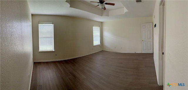 spare room featuring visible vents, baseboards, a raised ceiling, ceiling fan, and wood finished floors
