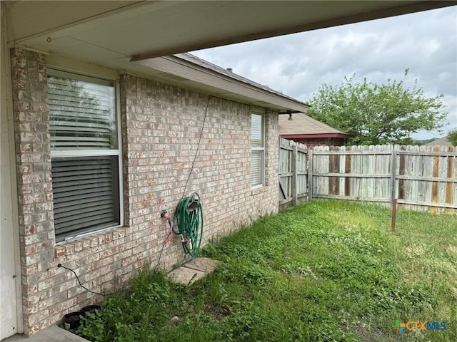 view of side of property with brick siding, fence, and a lawn