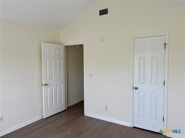 unfurnished bedroom featuring visible vents, baseboards, dark wood-style floors, and lofted ceiling