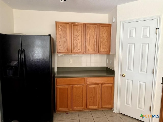 kitchen with tasteful backsplash, brown cabinetry, dark countertops, and black fridge