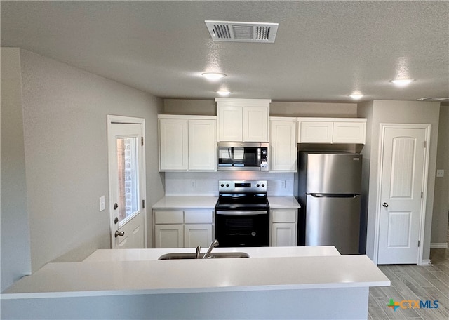 kitchen with sink, white cabinets, a textured ceiling, and appliances with stainless steel finishes