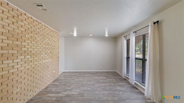 empty room featuring baseboards, brick wall, visible vents, and wood finished floors