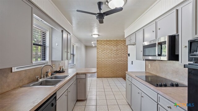 kitchen featuring ceiling fan, black electric stovetop, a sink, brick wall, and stainless steel microwave