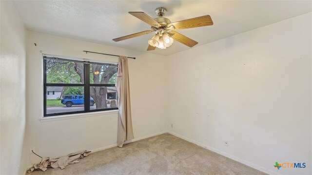 empty room featuring baseboards, ceiling fan, and light carpet