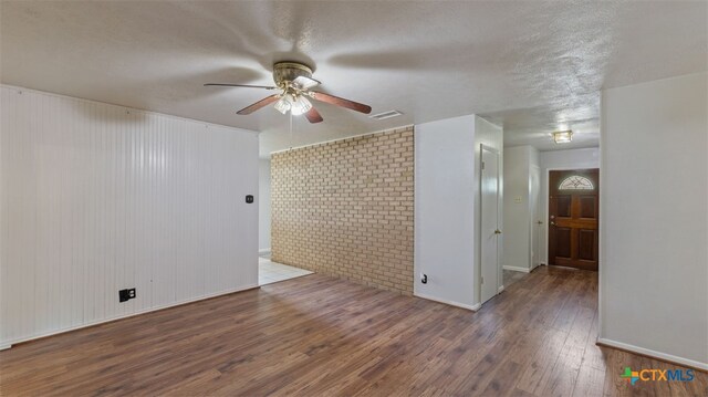 unfurnished room featuring visible vents, wood finished floors, brick wall, baseboards, and ceiling fan