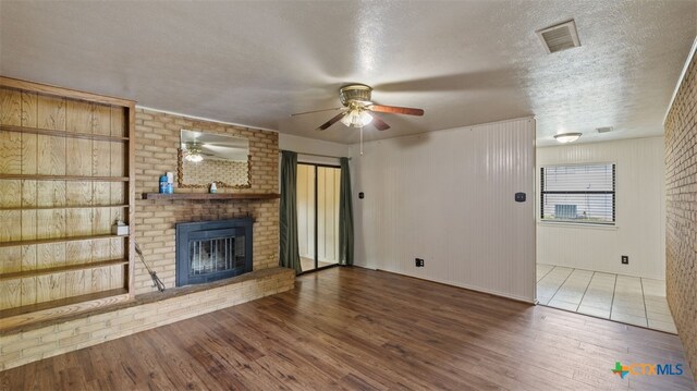 unfurnished living room featuring a ceiling fan, a textured ceiling, visible vents, a fireplace, and wood finished floors