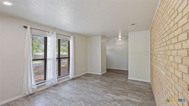 spare room featuring baseboards, brick wall, visible vents, and wood finished floors
