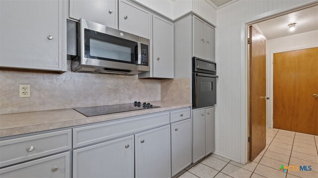 kitchen with light countertops, backsplash, light tile patterned floors, and black appliances