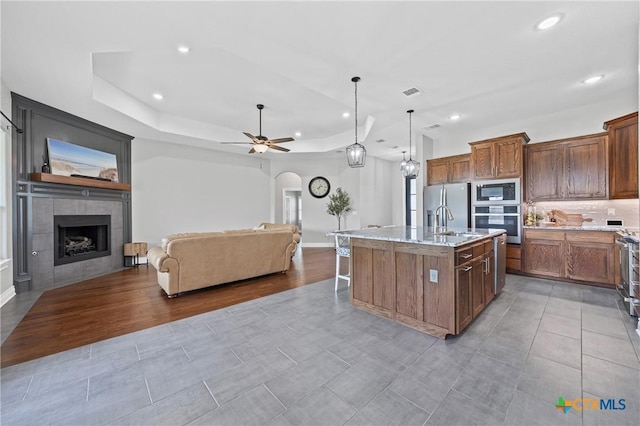 3631 Morgan Mill Rd, Kempner, TX 76539 - kitchen with stainless steel appliances, open floor plan, a fireplace, a center island with sink, and a ceiling fan