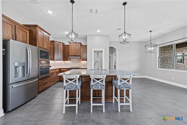 3631 Morgan Mill Rd, Kempner, TX 76539 - kitchen featuring appliances with stainless steel finishes, decorative backsplash, a breakfast bar area, arched walkways, and a kitchen island with sink