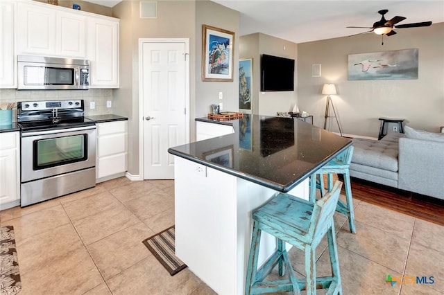 kitchen featuring ceiling fan, light tile patterned floors, a breakfast bar area, white cabinets, and appliances with stainless steel finishes