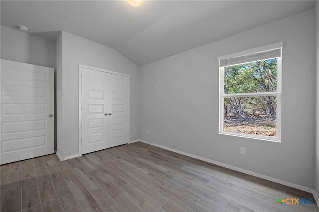 unfurnished bedroom featuring lofted ceiling, a closet, baseboards, and wood finished floors