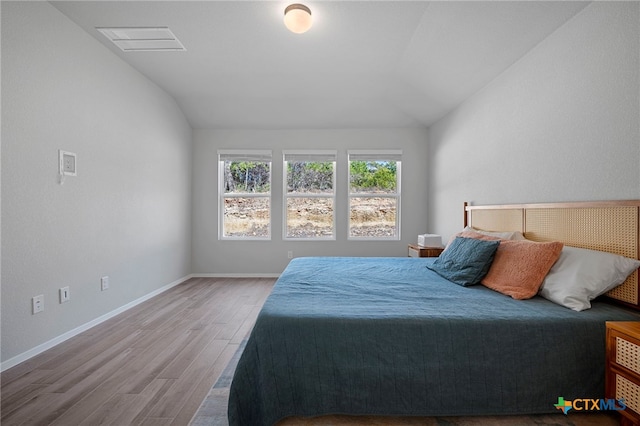 bedroom featuring lofted ceiling, visible vents, baseboards, and wood finished floors