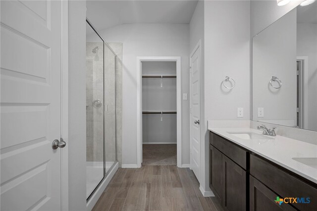 bathroom featuring double vanity, a stall shower, wood finished floors, a walk in closet, and a sink