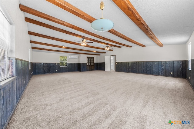 unfurnished living room with wood walls, carpet, a textured ceiling, and beam ceiling