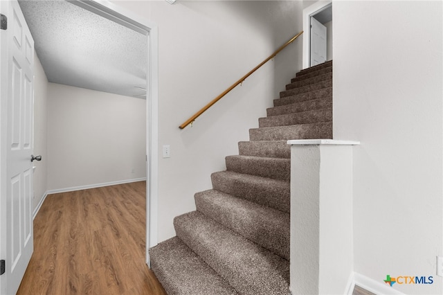 staircase with wood-type flooring and a textured ceiling