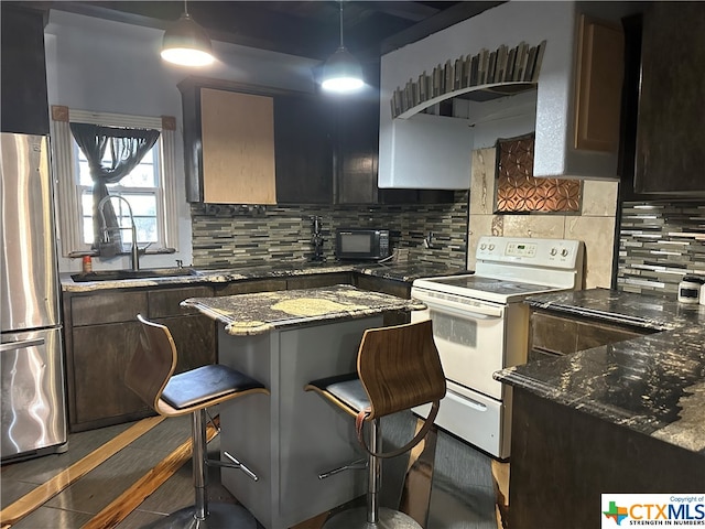 kitchen with sink, a breakfast bar area, tasteful backsplash, stainless steel fridge, and white electric stove