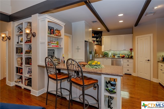 kitchen with beamed ceiling, white cabinetry, appliances with stainless steel finishes, a kitchen breakfast bar, and dark hardwood / wood-style flooring