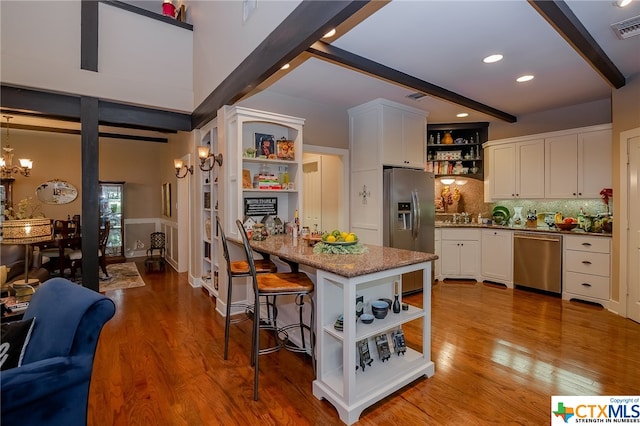 kitchen with light hardwood / wood-style flooring, beamed ceiling, appliances with stainless steel finishes, and white cabinets