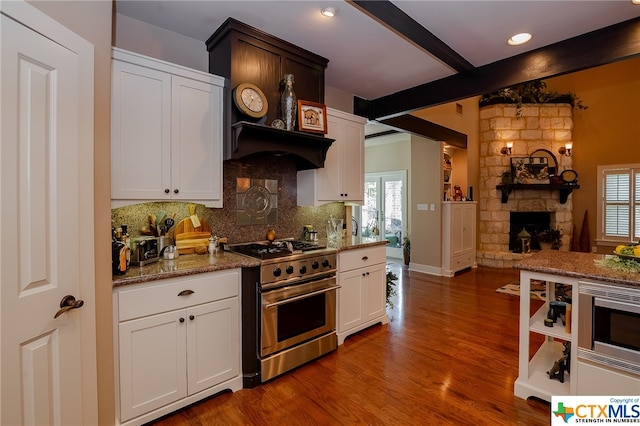 kitchen with stainless steel appliances, beamed ceiling, dark hardwood / wood-style floors, a stone fireplace, and white cabinets