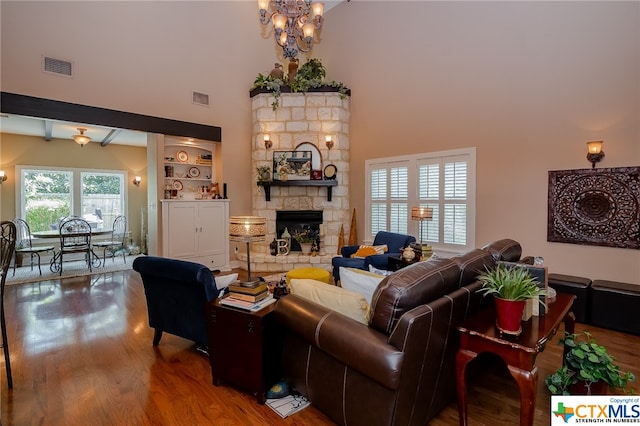 living room with a stone fireplace, hardwood / wood-style flooring, a chandelier, high vaulted ceiling, and beamed ceiling