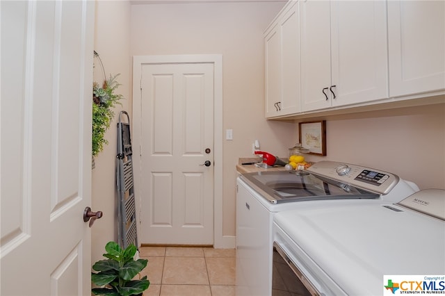 clothes washing area with cabinets, light tile patterned floors, and washer and dryer