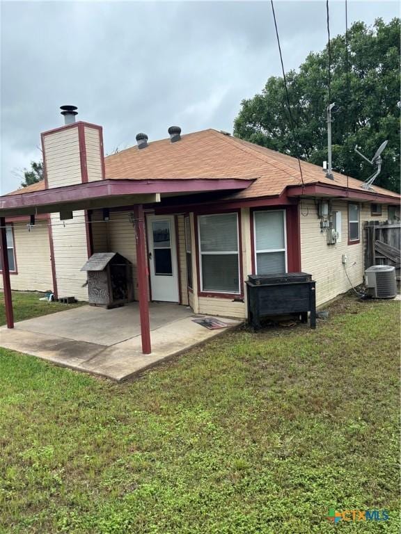 rear view of property featuring central AC unit, a patio, and a lawn