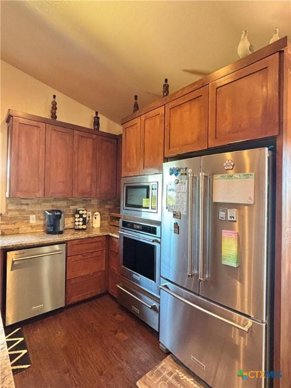 174 Riley Ln, Port Oconnor, TX 77982 - kitchen with appliances with stainless steel finishes, vaulted ceiling, decorative backsplash, brown cabinets, and dark wood-style flooring