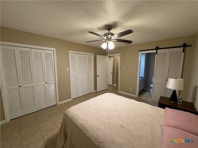 bedroom with ceiling fan, a barn door, tile patterned floors, ensuite bath, and multiple closets