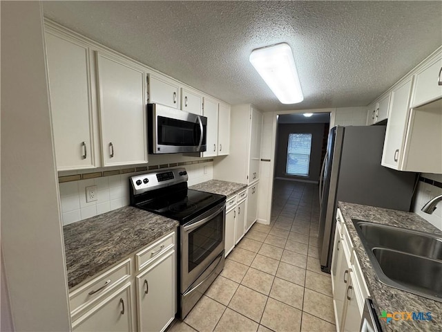 kitchen with a textured ceiling, white cabinets, appliances with stainless steel finishes, sink, and light tile patterned floors