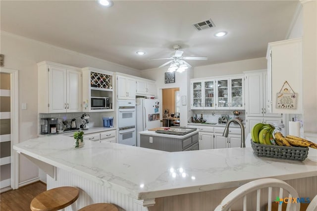 kitchen featuring tasteful backsplash, a breakfast bar area, white cabinets, kitchen peninsula, and white appliances