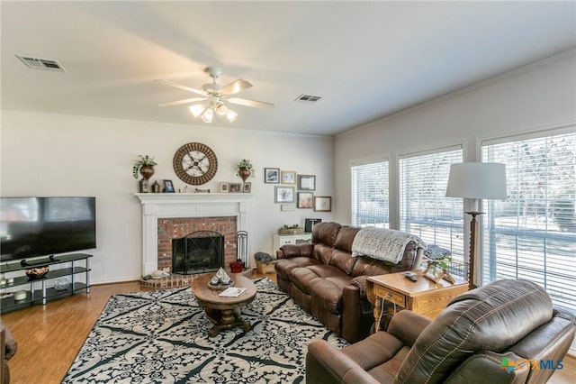 living room featuring a brick fireplace, crown molding, light hardwood / wood-style floors, and ceiling fan