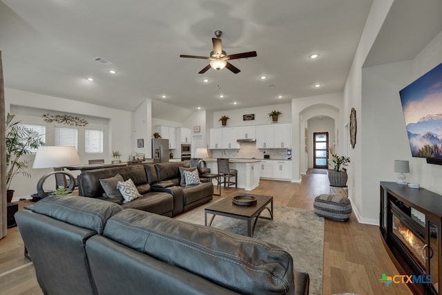 living room with a wealth of natural light, ceiling fan, vaulted ceiling, and light hardwood / wood-style flooring