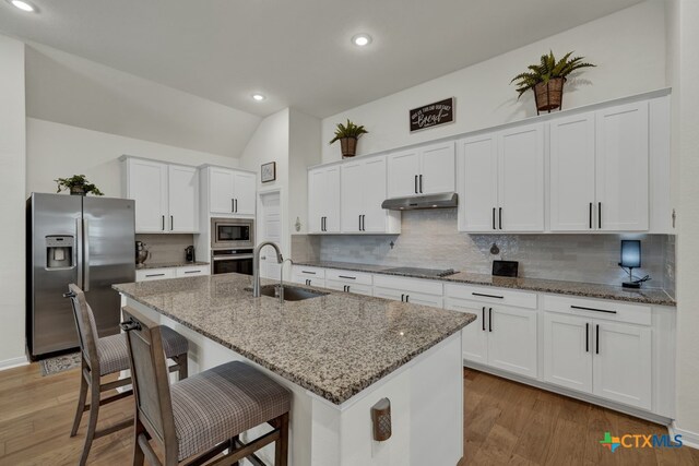 kitchen with stainless steel appliances, white cabinetry, sink, an island with sink, and vaulted ceiling